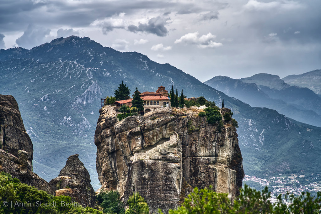 Monastery on a huge rock in Meteora, Greece with mountain range and dramatic clouds